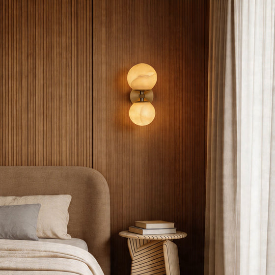 Double globe wall light glowing on a slatted wood wall above a cozy modern bedside table set.