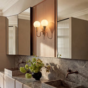 Double globe wall sconce above a bathroom vanity with warm lighting and brass finish.