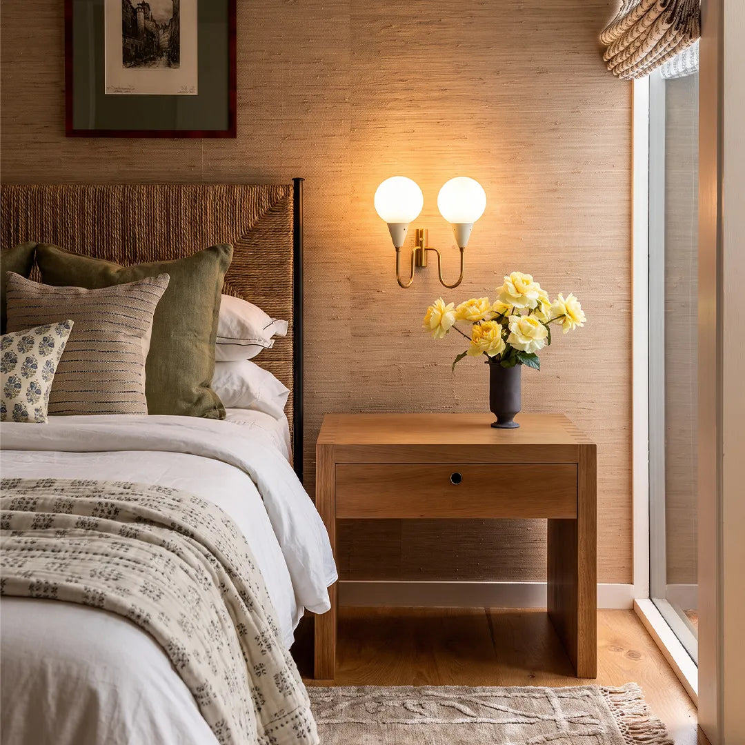 Double globe wall sconce above a bedside table with warm lighting in a cozy bedroom.