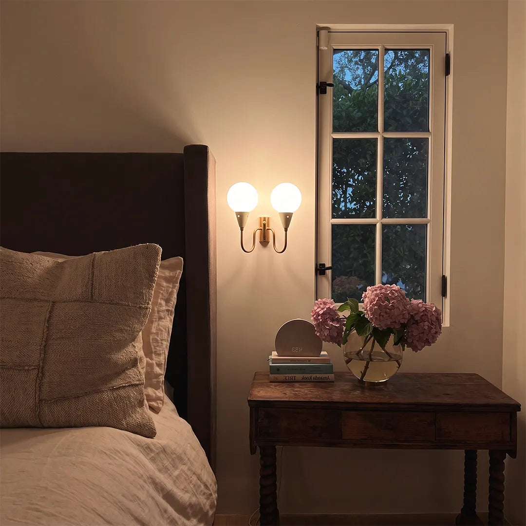 Double globe wall sconce beside a bed and nightstand with soft warm illumination.