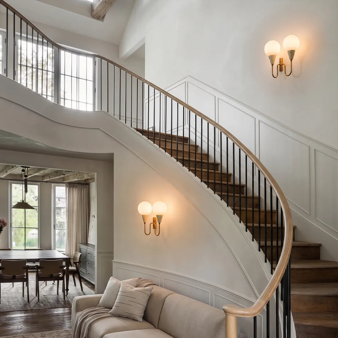 Double globe wall sconce mounted along a curved staircase wall in an elegant foyer.