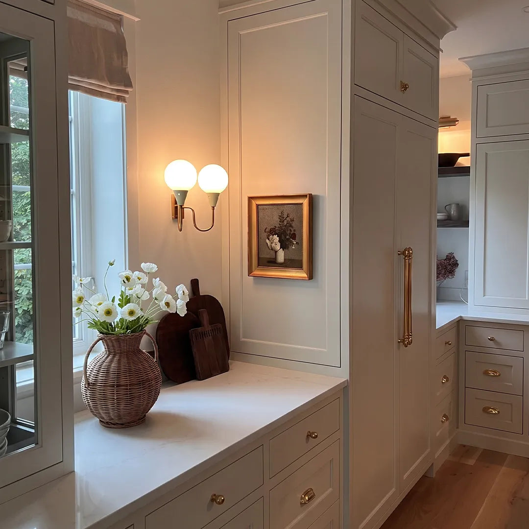 Double globe wall sconce mounted beside a window seat in a bright transitional interior.