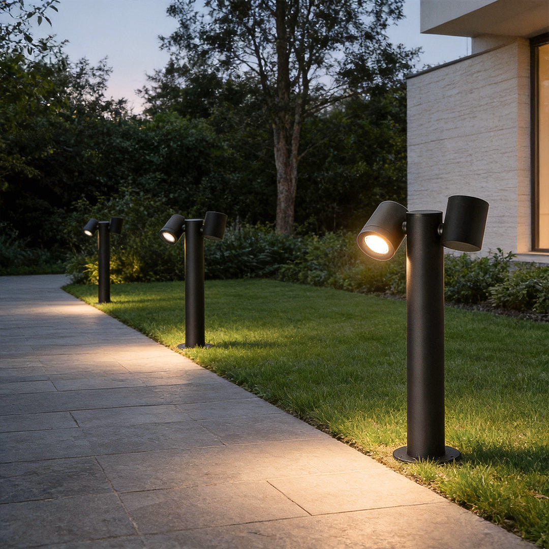 Double light bollard light providing soft illumination along a garden walkway.