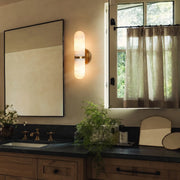 Double light wall sconce installed beside a bathroom mirror with warm ambient lighting.