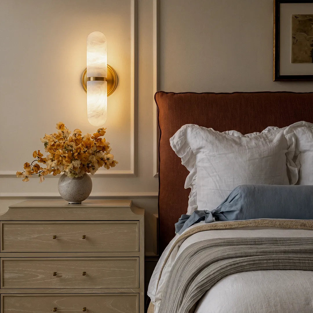 Double light wall sconce mounted beside a bed with soft upward and downward lighting.