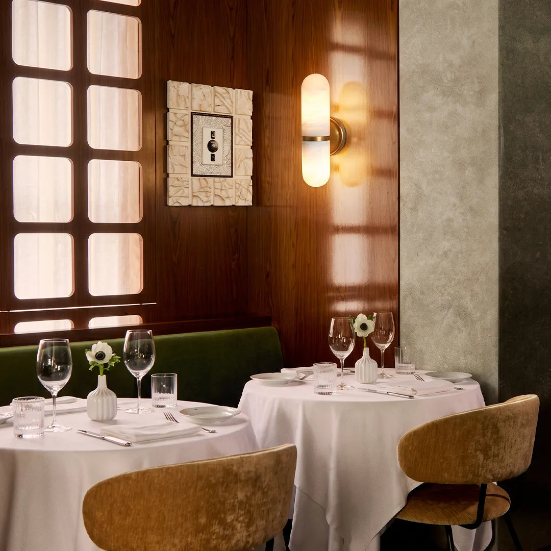Double light wall sconce adding elegant illumination to a restaurant dining area with wood panel walls.