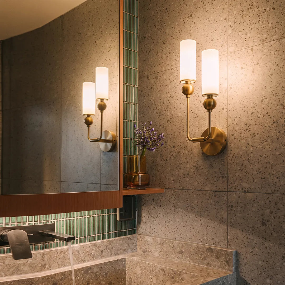 Double sconce wall light beside a bathroom mirror with twin frosted glass shades and warm glow.