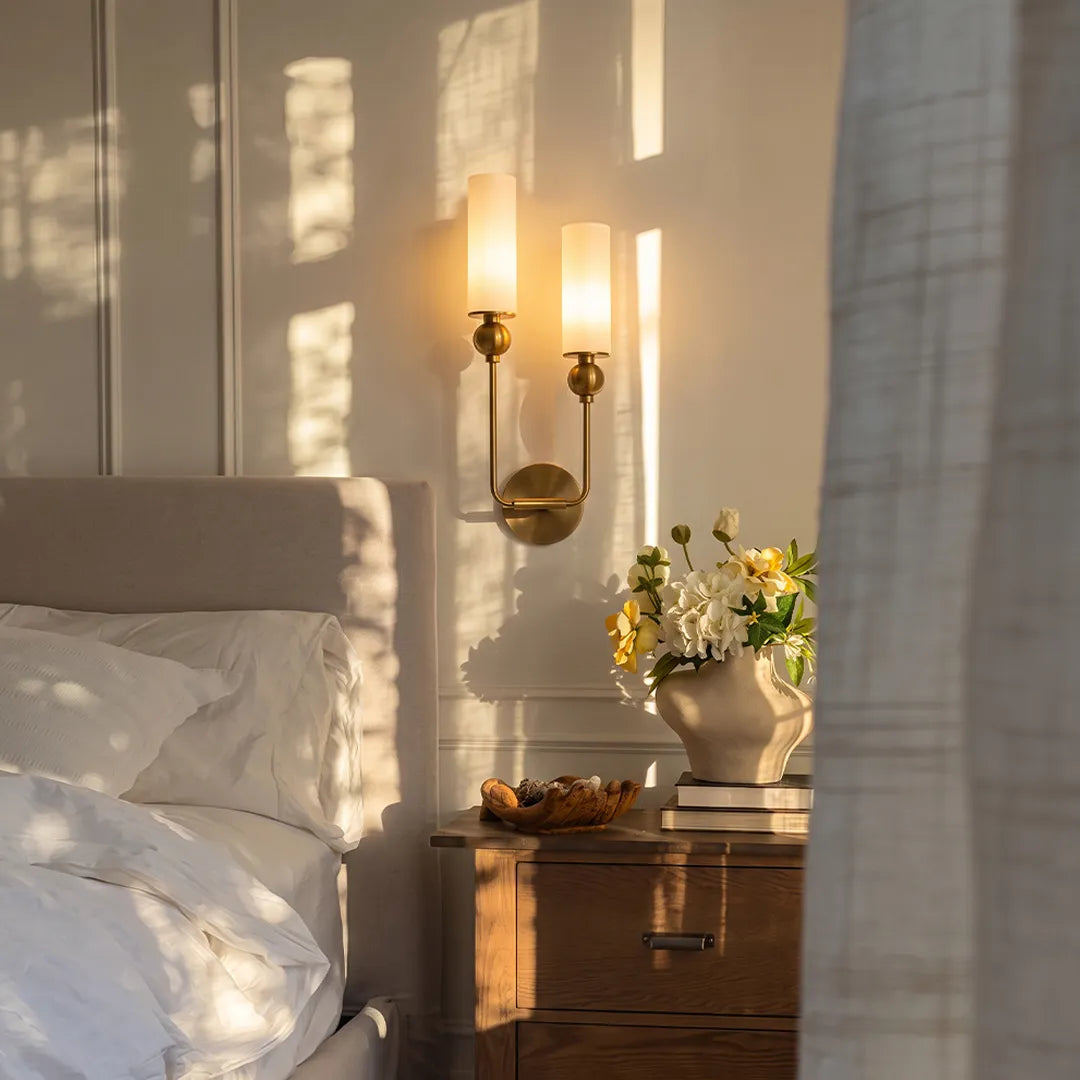 Double sconce wall light mounted beside a bed with two frosted glass shades and warm ambient lighting.