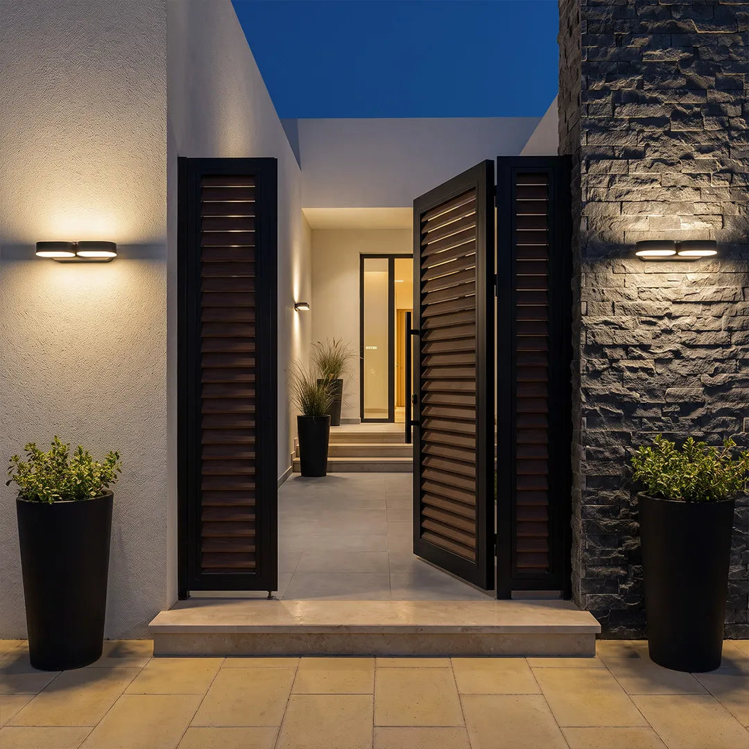 Double wall lights installed beside an entry walkway, featuring two adjustable heads and a black modern design.