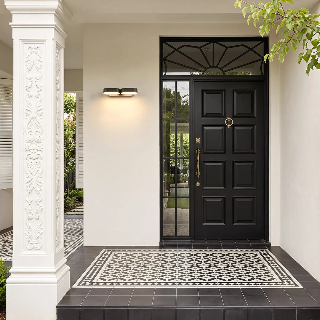 Double wall lights installed beside a modern front door, featuring two adjustable light heads and a sleek black finish.