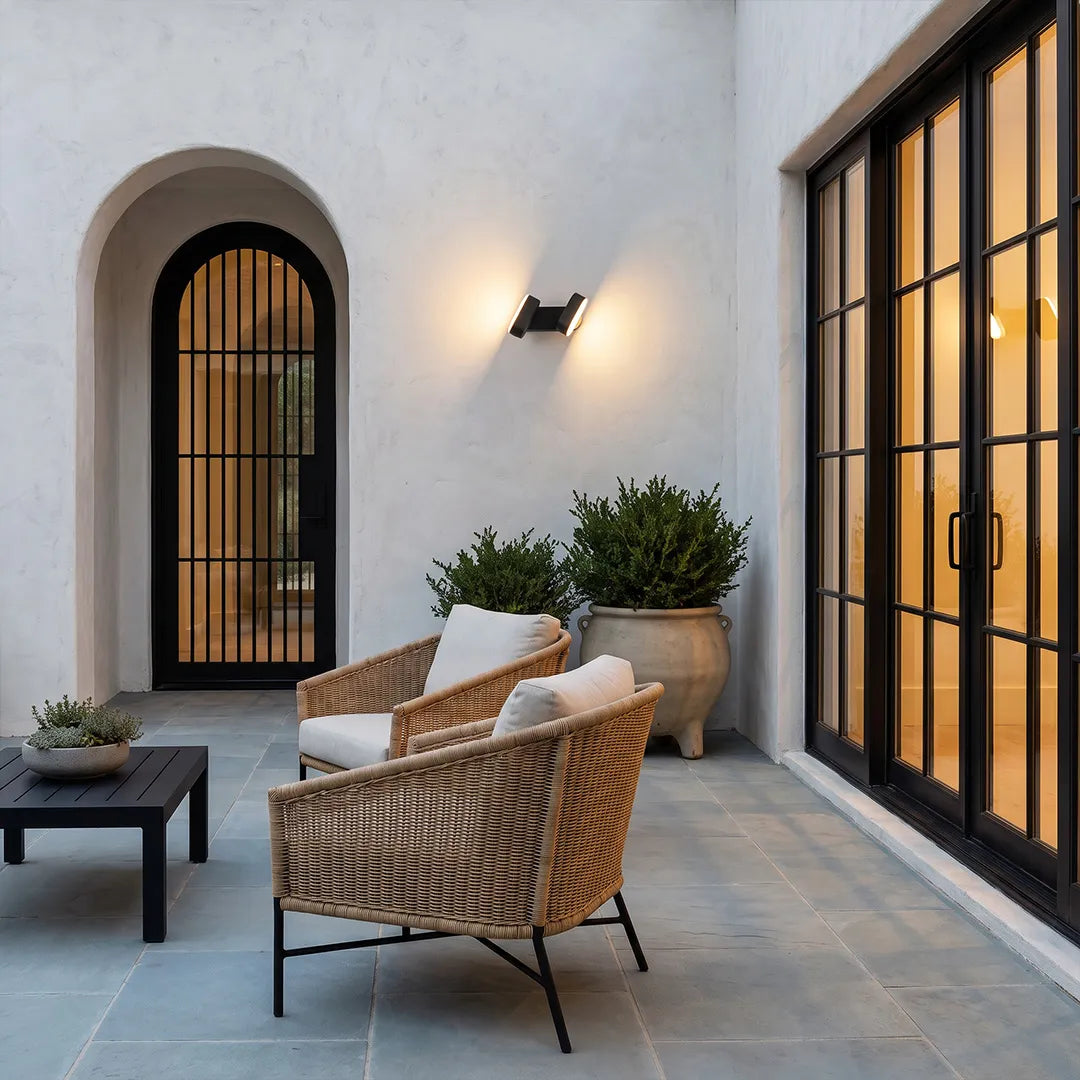 Double wall lights adding warm accent lighting to a modern patio with wicker seating and arched doors.