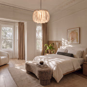 Drum light chandelier hanging above a bed in a bright bedroom with soft neutral decor.