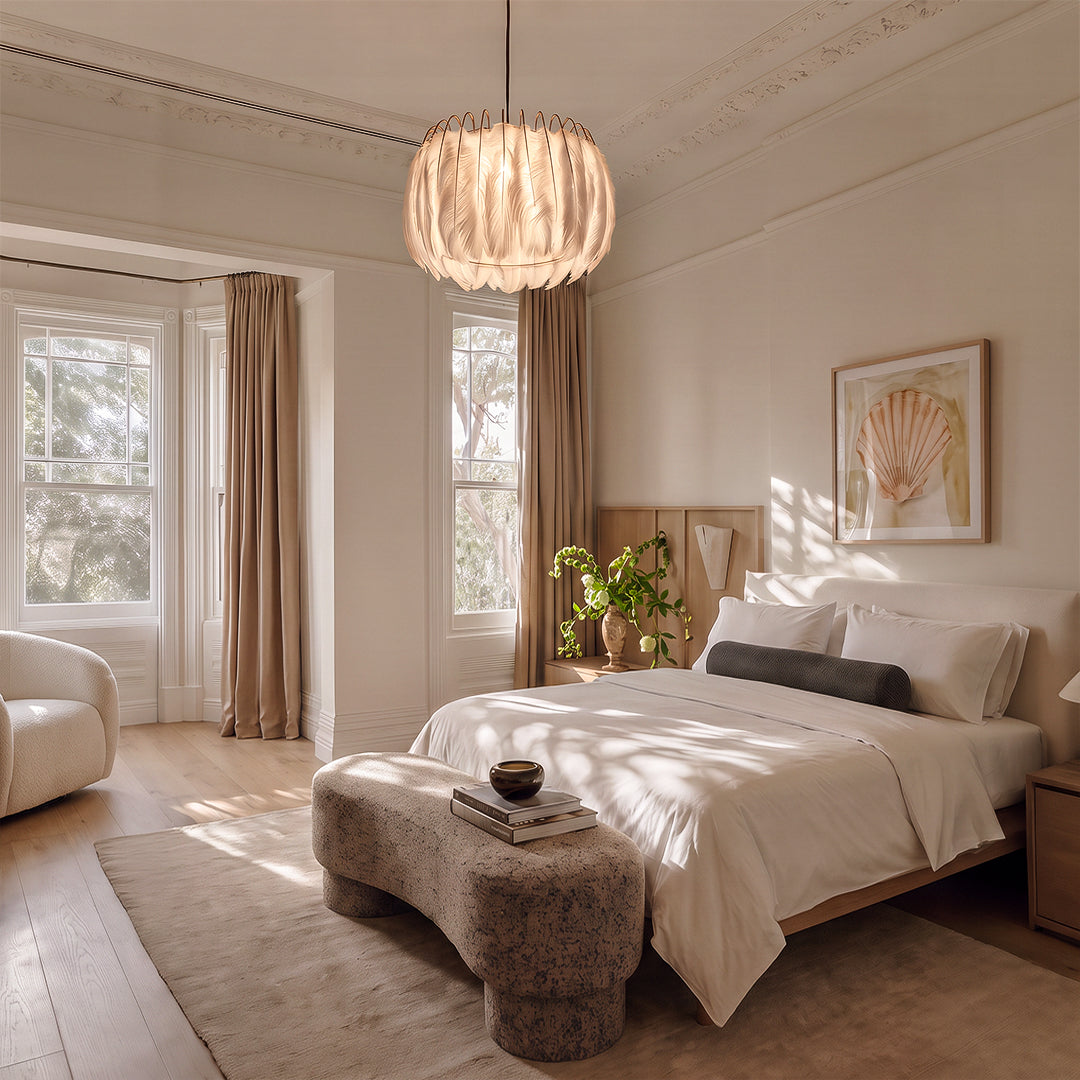 Drum light chandelier hanging above a bed in a bright bedroom with soft neutral decor.
