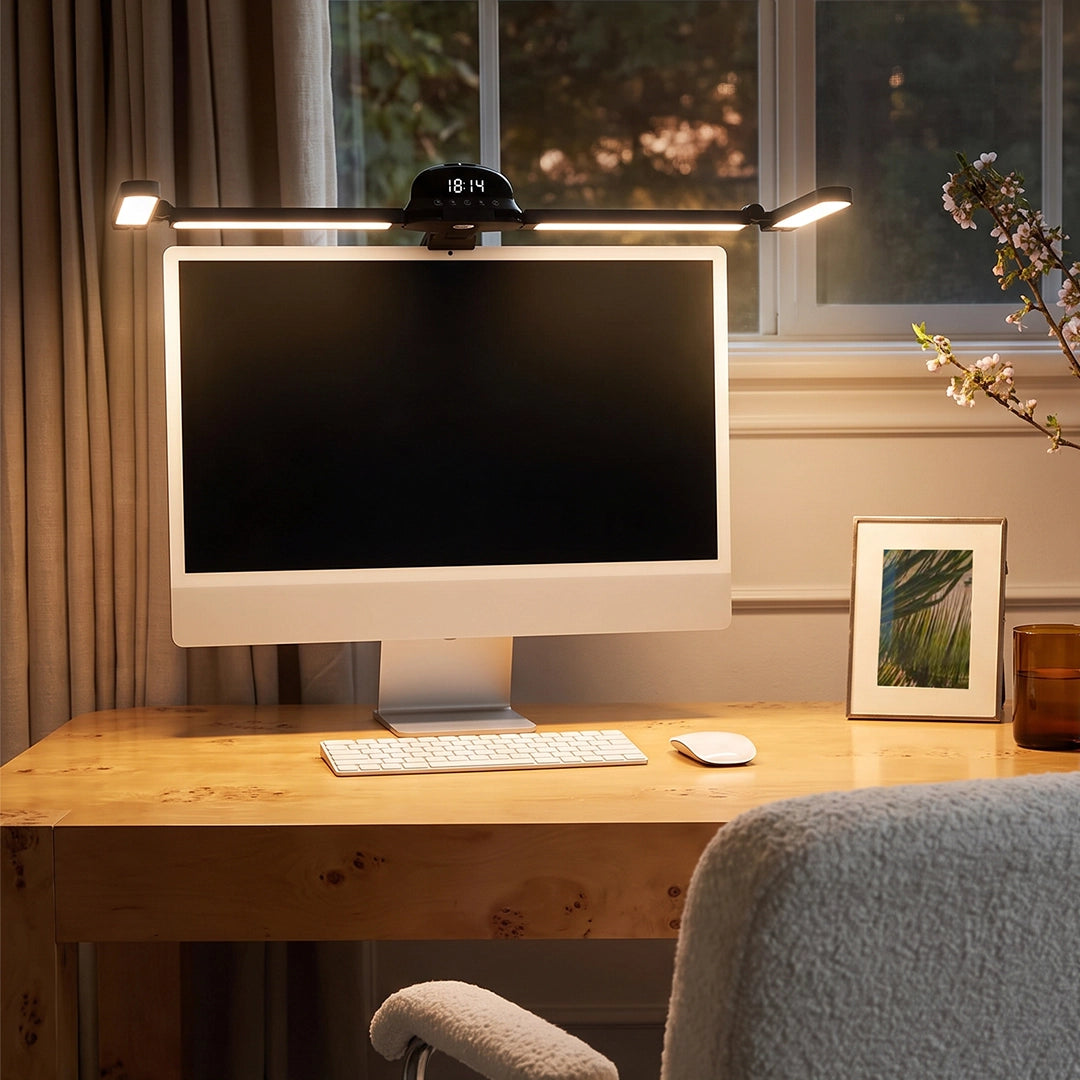 Dual monitor light bar illuminating a desktop computer setup on a warm wooden desk by the window.