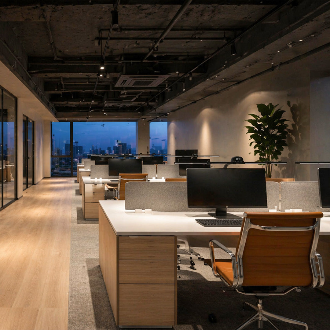 Dual monitor light bars illuminating computer workstations in a modern open-plan office at night.