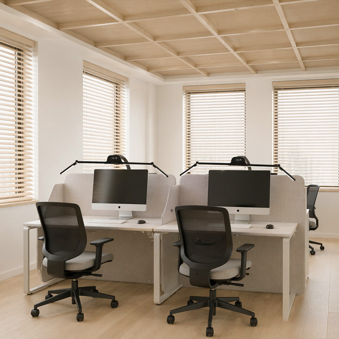 Dual monitor light bars installed on two computer screens in a bright shared office workspace.