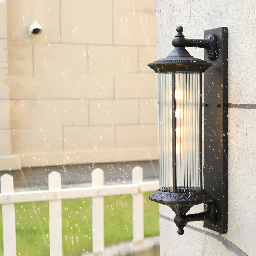 Black decorative outdoor wall sconce with vertical glass cylinder mounted on residential exterior wall
