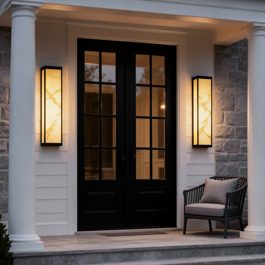 Econic outdoor wall light mounted beside black double doors, creating elegant entryway lighting on a white exterior facade.