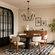 Elegant French style chandelier with an antique bronze finish and scrolling arms, hanging above a contemporary round dining table.