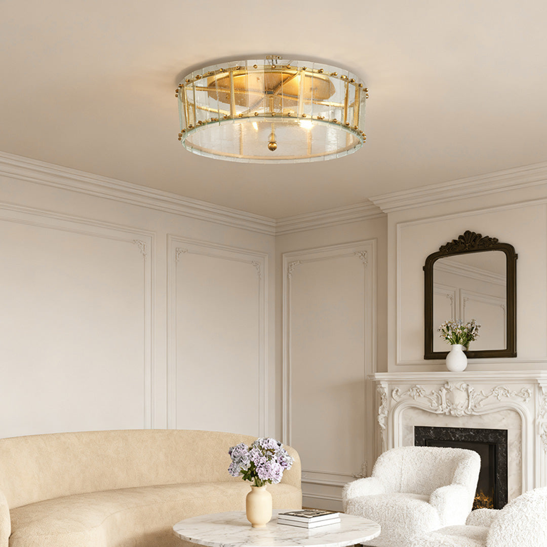 Elegant flush mount gold light with a beveled glass shade, centered in a luxurious living room above a white curved sofa and fireplace.