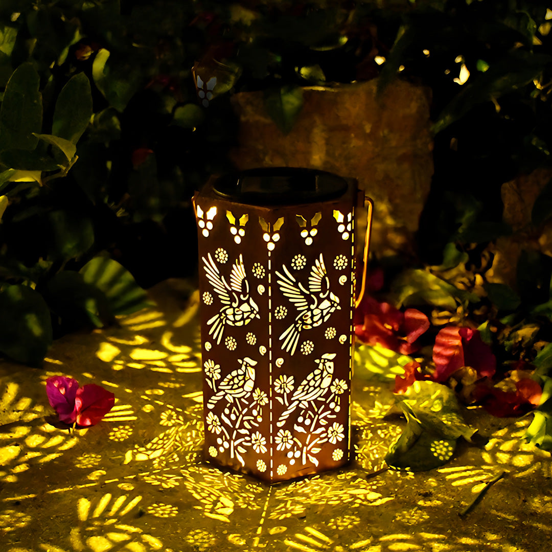 Elegant bird and flower pattern on a red outdoor lantern creating beautiful shadows on garden foliage.