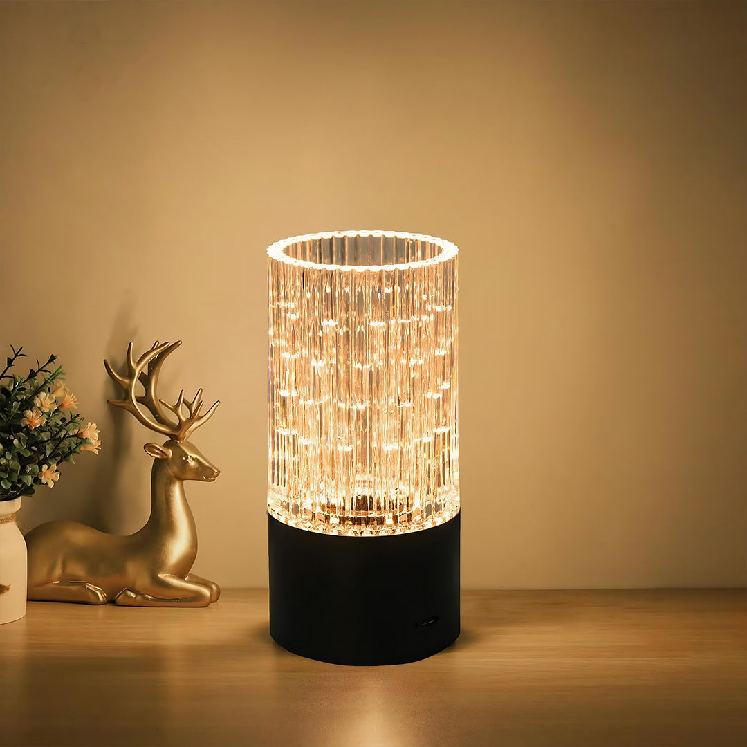 Elegant deco table lamp with a black base and clear crystal cylinder creating a beautiful light pattern on a wooden surface.