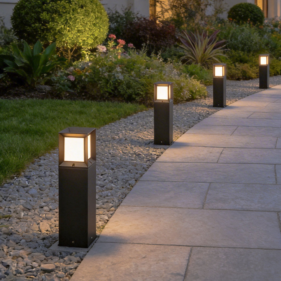 Row of elegant black outdoor bollard lights illuminating a stone garden pathway during evening.