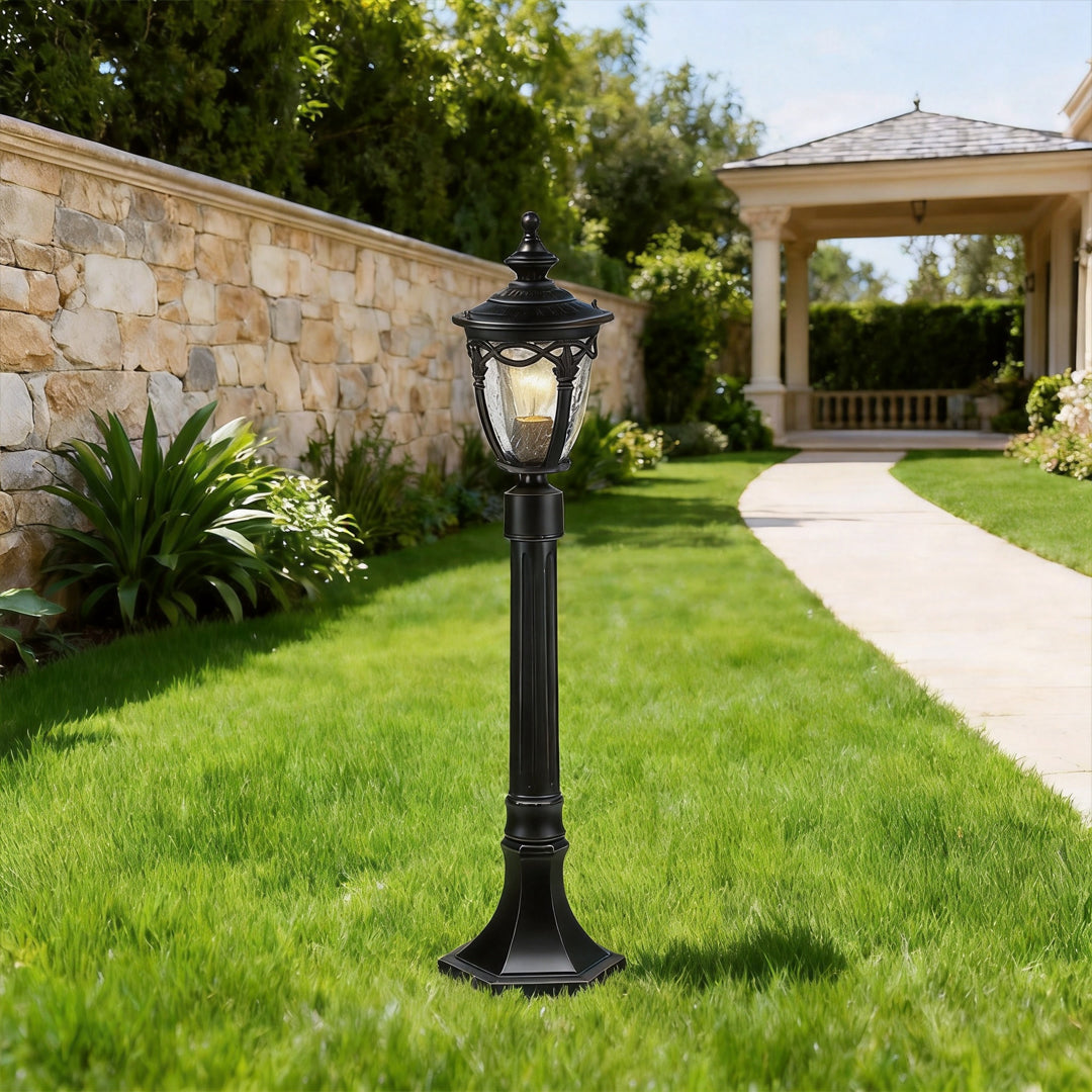An elegant black outdoor light post installed on a manicured lawn near a stone wall and walkway