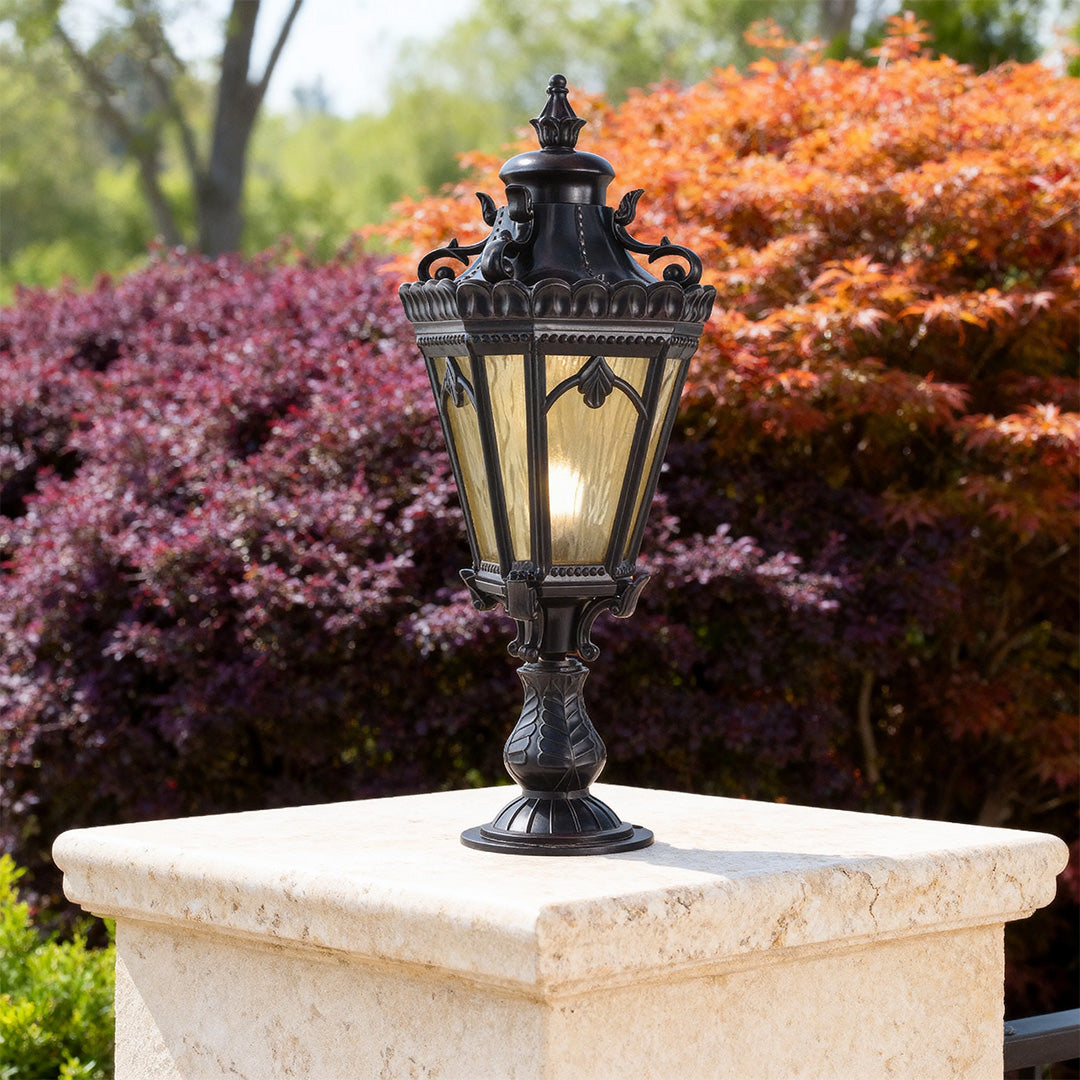 Elegant black outdoor pillar light mounted on white stone pier with lush green foliage backdrop