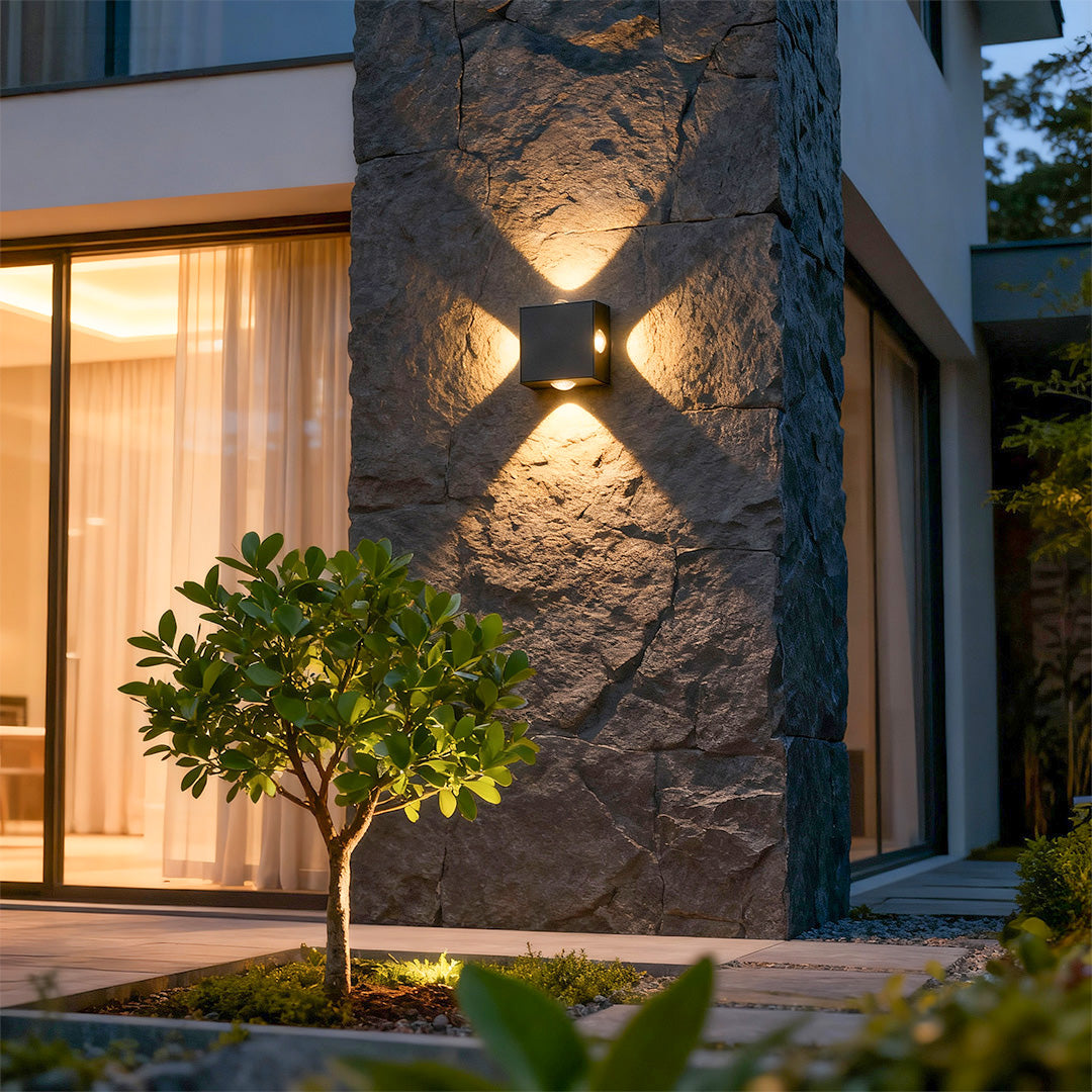 Elegant black outdoor sconce light with glass shade chandelier design creating dramatic cross-pattern illumination on dark stone facade.