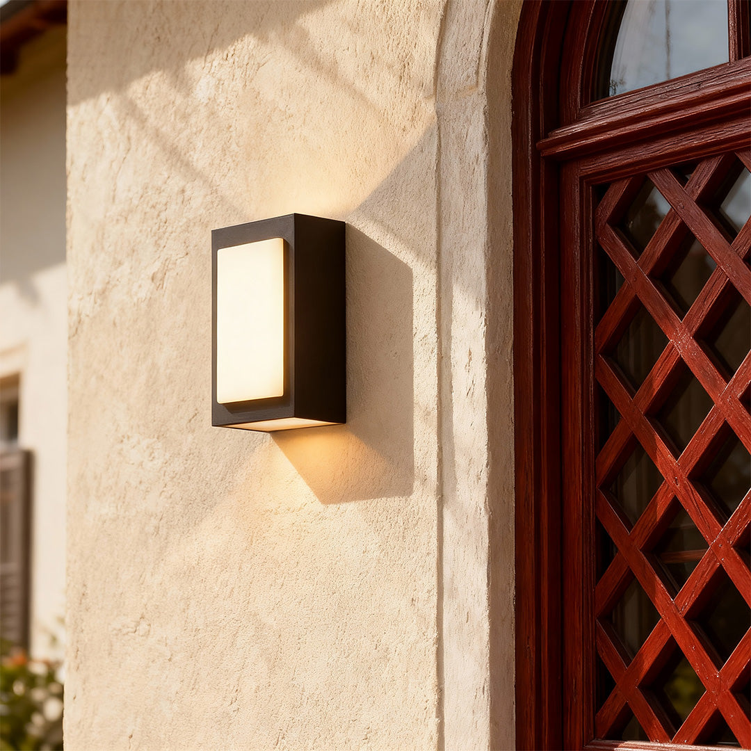 Elegant black sconce wall lights with glass shade chandelier design illuminating textured stucco exterior beside decorative lattice.
