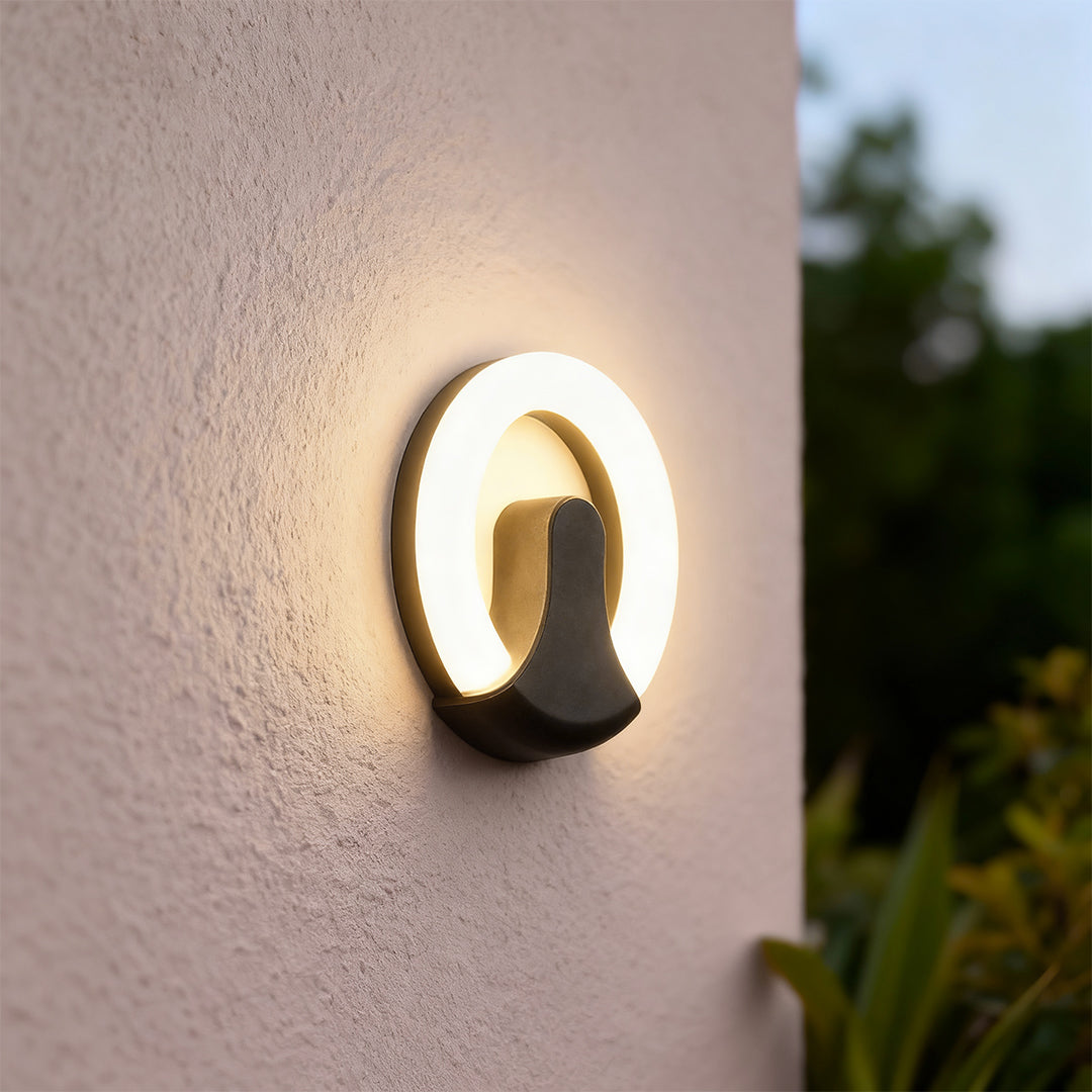 Elegant black wall sconce light with glass shade chandelier design illuminating textured stucco exterior with soft halo effect.