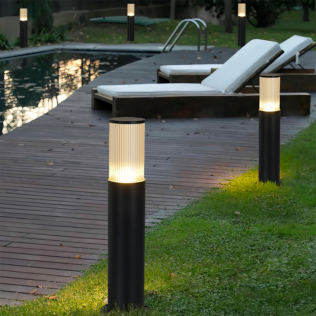 Elegant bollard path light fixtures lining a wooden pool deck and grassy area for nighttime ambiance.