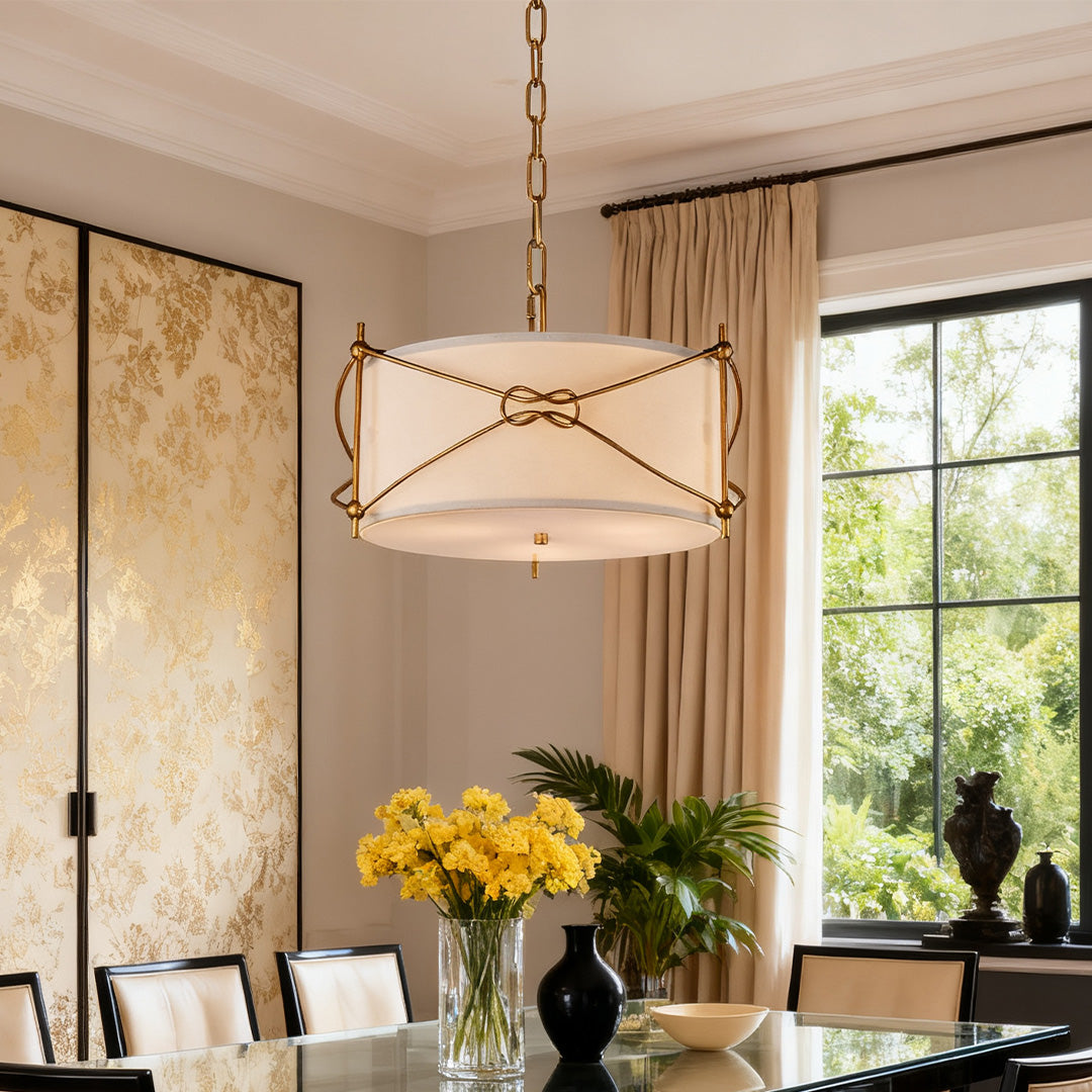 Elegant white drum pendant light with decorative brass chain detail, illuminating a dark glossy dining table and gold patterned wall.