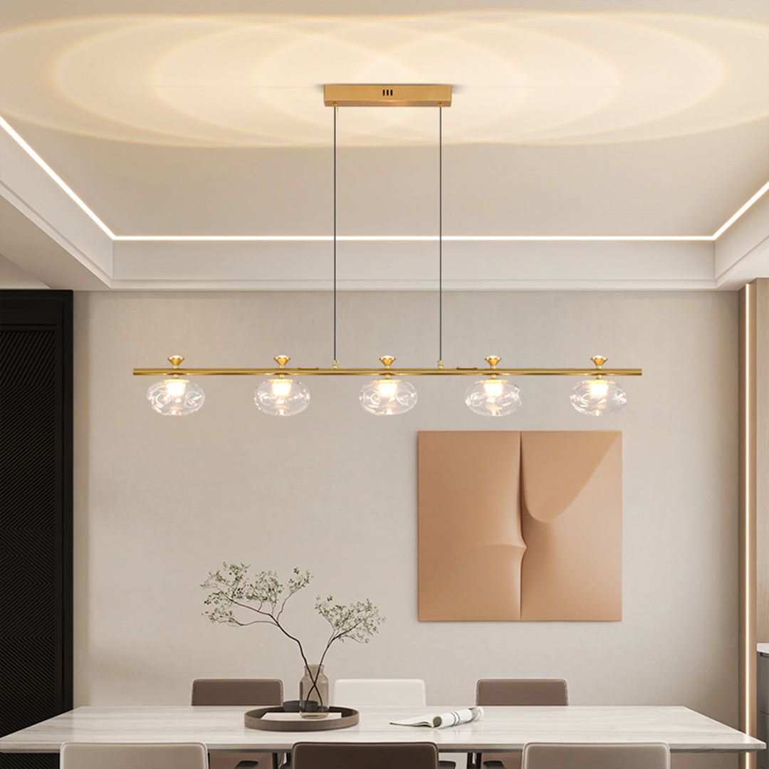 Elegant linear glass chandelier with brass finish suspended over contemporary dining area