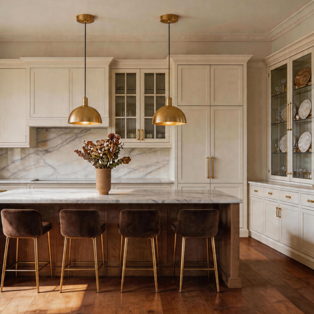 Elegant brass pendant lighting hanging in a warm white kitchen above a marble breakfast bar ok