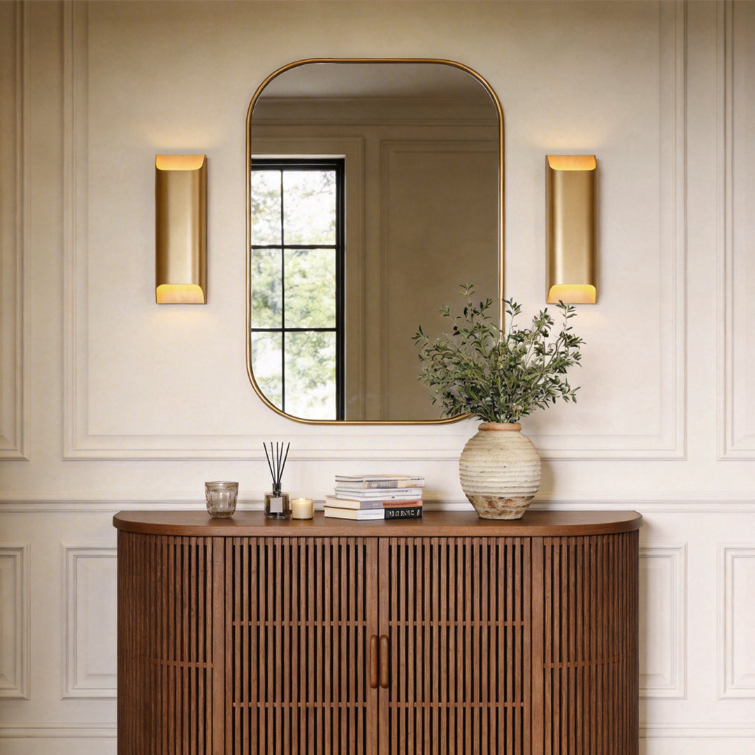 Elegant brass wall lights flanking a large mirror above a wood sideboard in a classic hallway.