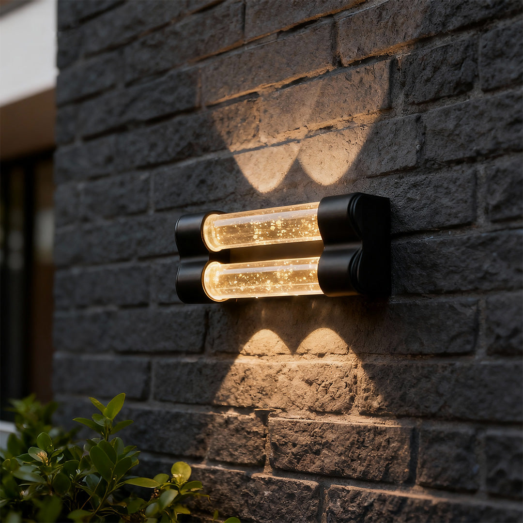 Elegant crystal wall sconce light fixture with glass shade chandelier design illuminating dark textured brick exterior wall.