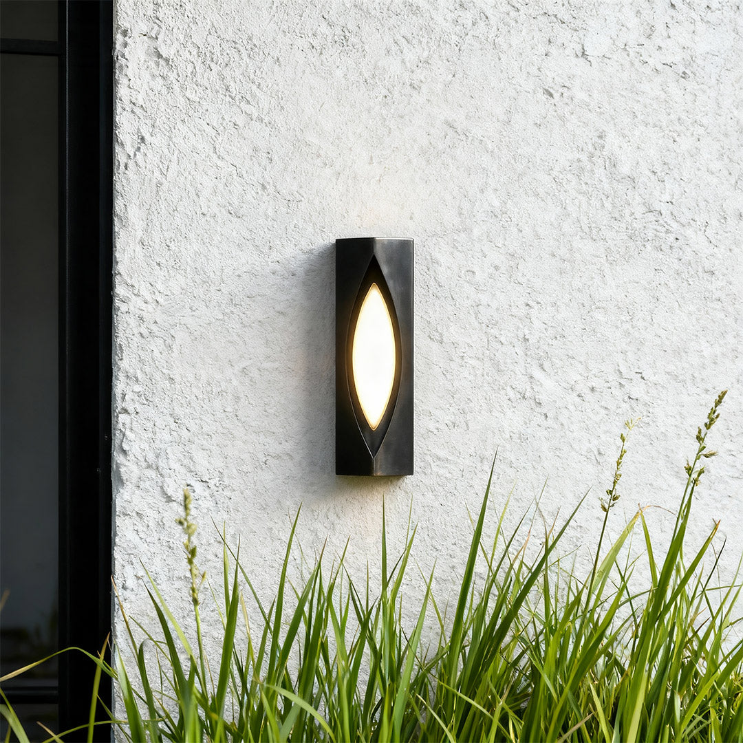 Elegant decorative wall sconce lighting with glass shade chandelier design illuminating white exterior wall with ornamental grasses.