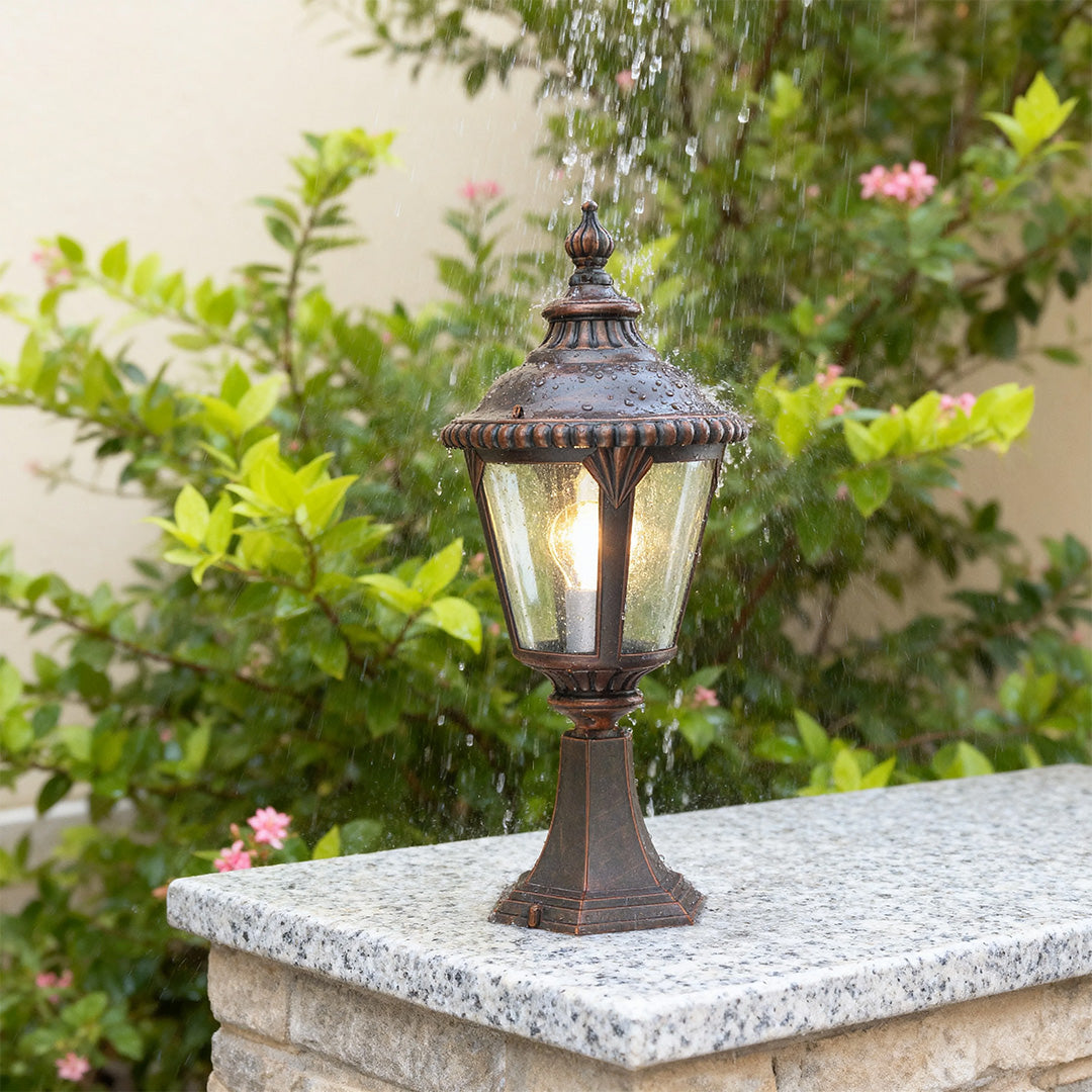 Elegant fence pillar light standing on granite post with pink flowers and soft focus garden