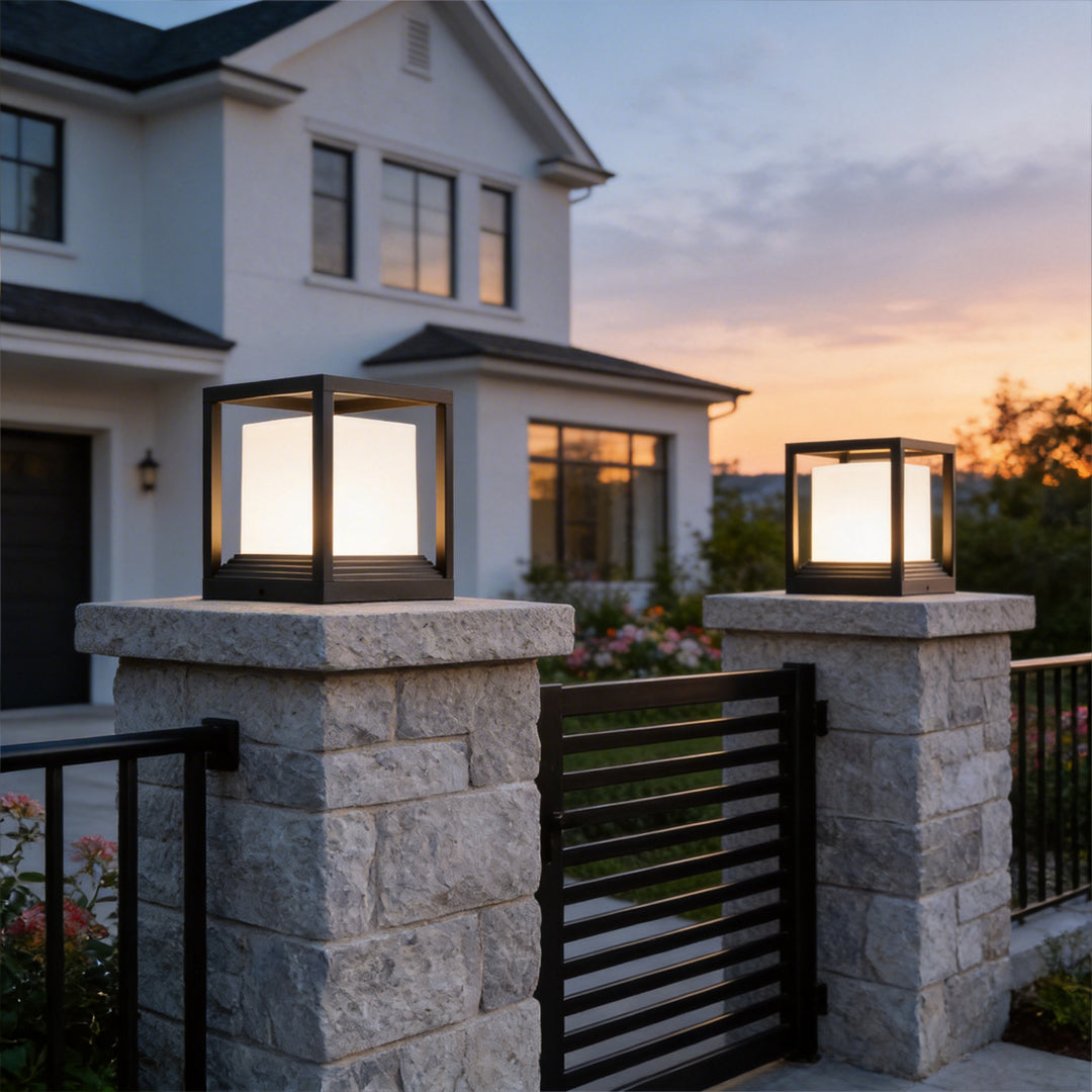 Elegant garden pedestal lights glowing on stone gate posts in front of a luxury white house.