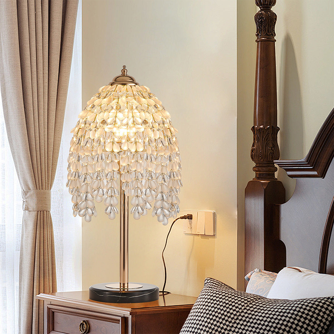Elegant gold bedside table lamp featuring glass shade chandelier design illuminating traditional bedroom with four-poster bed.