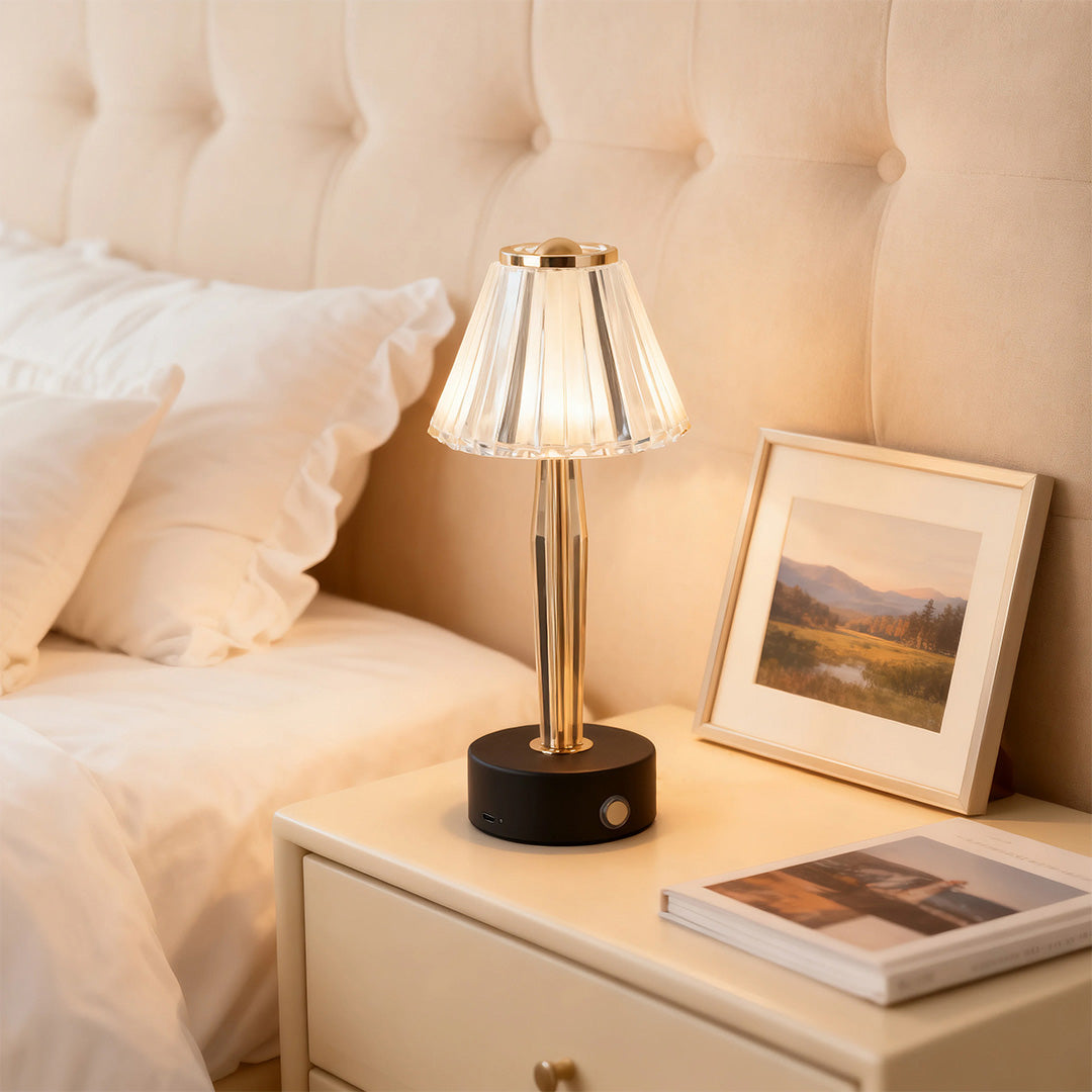 Elegant gold and black classic table lamp with a pleated glass shade providing a cozy glow on a white nightstand.