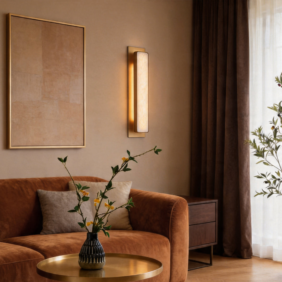 Elegant gold wall light fixture illuminating a warm living room with brown sofa and artwork.