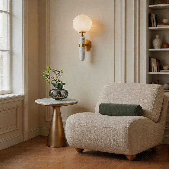 Elegant gold wall sconce lighting with a white globe shade in a cozy modern reading corner.