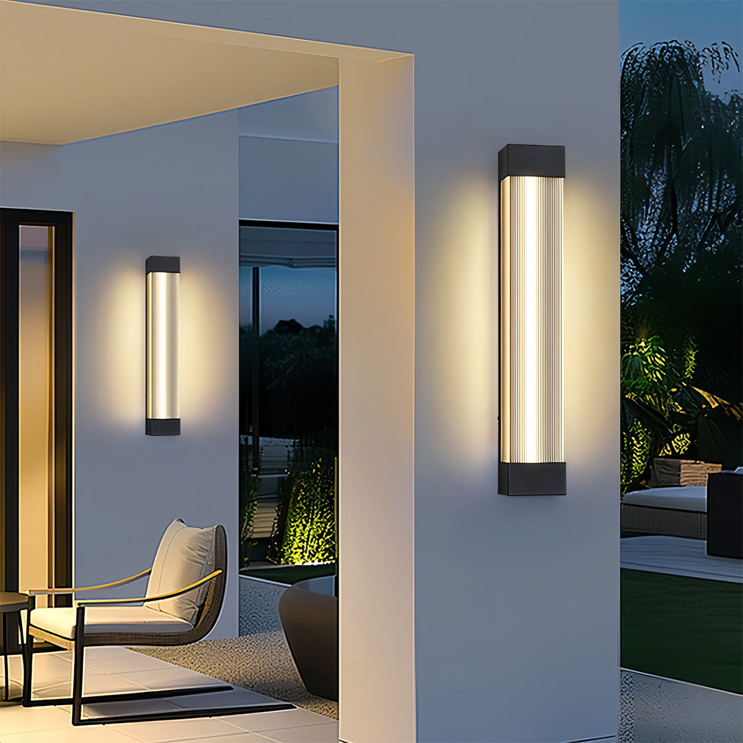 Elegant linear outdoor sconce fixtures enhancing the ambiance of a covered patio and walkway at night.
