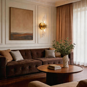 Elegant modern crystal wall light glowing on a paneled beige wall in a luxury living room area.