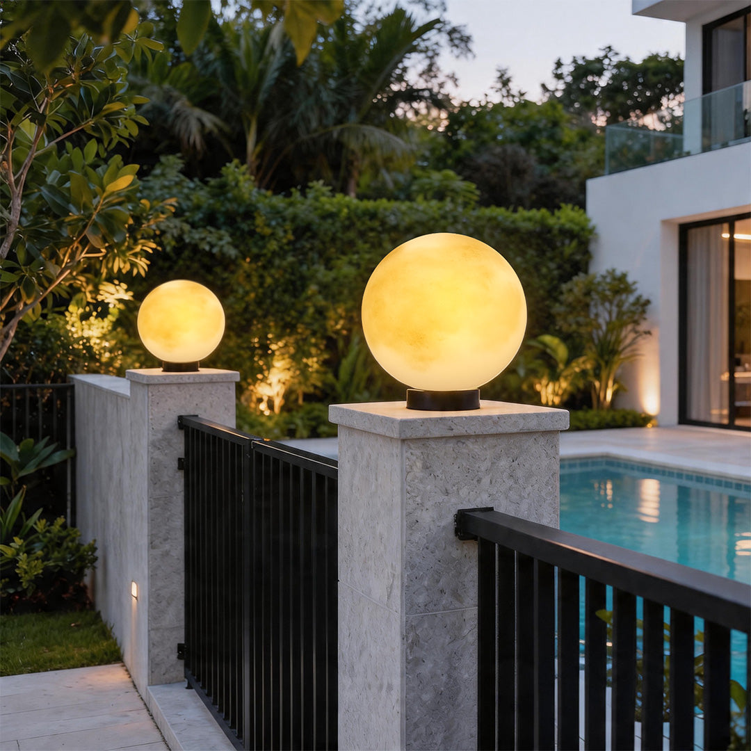 Elegant moon pillar lights glowing on stone pillars at a luxury villa entrance near the pool.