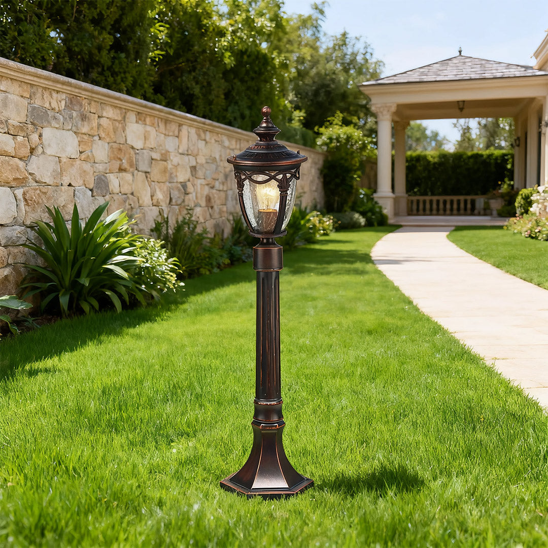 Elegant outdoor light bollard standing on green lawn near stone archway entrance and pathway