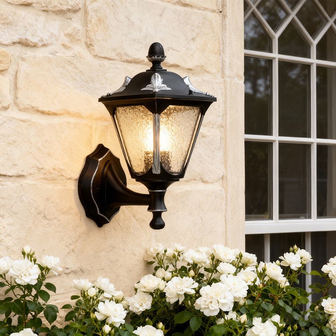 Elegant outdoor light for wall illuminating beige stone facade with white flowers below